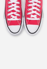 Punaiset kangastossut, joissa on valkoiset nauhat, mustat kumipohjat ja valkoiset kärjet, klassisella matalalla designilla.