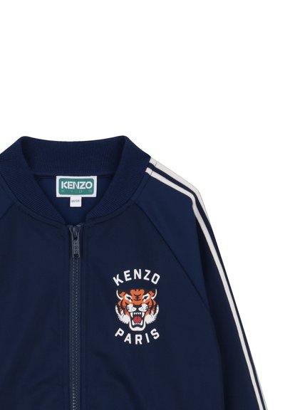 Veste zippée pour enfants bleu marine avec des bandes blanches sur les manches et un logo de tigre rugissant avec le texte "KENZO PARIS" sur la poitrine.
