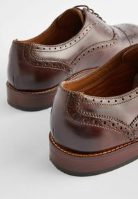 Brown leather shoes with perforated detailing, rounded toe, and a sturdy, stacked heel. Features a smooth finish and lace-up design.
