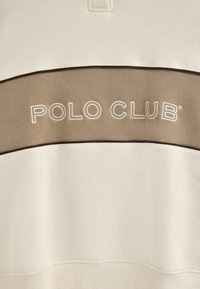 Felpa crema con un pannello beige su cui è ricamato in bianco "POLO CLUB". Il materiale sembra morbido; il design è semplice e sportivo.