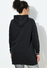 Felpa nera con cappuccio, vestibilità comoda, maniche lunghe e dettagli con strisce bianche sui polsini. Tessuto morbido e orlo posteriore più lungo per una maggiore copertura.