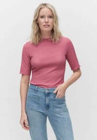 Dopasowany, teksturowany różowy top z krótkim rękawem, w połączeniu z jasnoniebieskimi spodniami o wysokim stanie, które mają kieszenie z przodu i z tyłu.