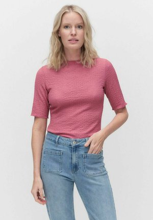 Fitted, strukturiertes pinkes Oberteil mit kurzen Ärmeln, kombiniert mit hellblauen, hochgeschnittenen Jeans mit vorderen und hinteren Taschen.