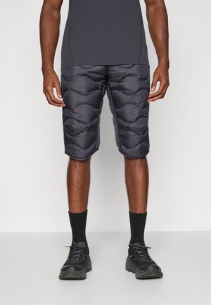 Pantaloni corti neri imbottiti con un design trapuntato e una superficie liscia, indossati con una maglietta grigia aderente e calze e scarpe da ginnastica nere.