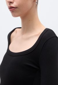 Μαύρο ριμπ μακρυμάνικο τοπ με ευρύ ντεκολτέ σε σχήμα στρογγυλής λαιμόκοψης. Μαλακή υφή και εφαρμοστή σχεδίαση που αναδεικνύει τους ώμους και την περιοχή του κολάρου.