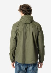Chaqueta ligera color verde oliva con capucha, puños elásticos y un corte relajado. Textura suave con mínimos detalles de costura.