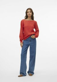 Rød ribbet striktrøje med bred udskæring og lange ærmer, parret med højtsiddende, lige blå jeans og brune flade sko.