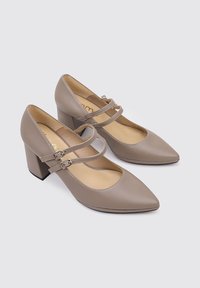 Talons beiges à bout pointu avec des talons carrés, deux brides réglables sur le dessus du pied et une texture lisse semblable au cuir.
