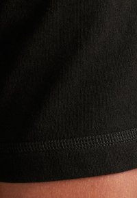 Čierna bavlnená T-shirt látka s hladkou textúrou a lemom, ktorý má pevné, rovné stehy pozdĺž spodného okraja.
