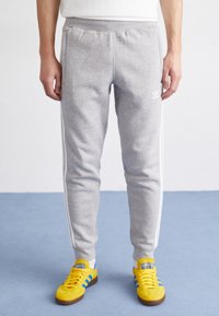 Sive trenirke s belimi črtami ob straneh, elastičnim pasom in majhnim logotipom na levi stegni, združene s svetlo rumenimi supergami.