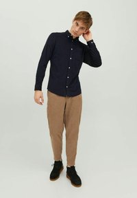 Camisa azul marino de botones con cuello y bolsillo en el pecho, combinada con pantalones de pana color marrón claro, ajustados y zapatos negros con suelas color crema.