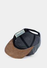 Baseball cap featuring a brown suede brim, gray fabric body, black accents, and a logo tag inside. Six ventilation eyelets are visible.