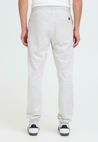Grijze joggingsbroek heeft een relaxte pasvorm, taps toelopende pijpen, een elastische tailleband en een achterzak. G draagt met zwart-witte sneakers.