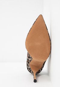 Chaussure à talon haut à bout pointu avec dessus imprimé léopard et semelle couleur tan, positionnée debout contre un fond blanc d'angle.