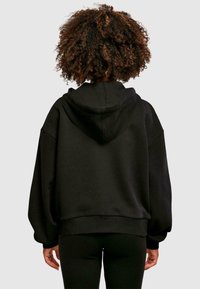 Black oversized hoodie with a spacious design, ribbed cuffs, and a hood, featuring a soft, smooth texture, worn with slim black leggings.