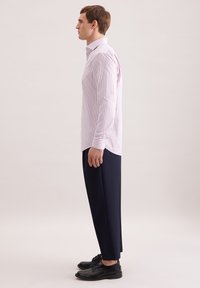 Camicia a righe rosa e bianca, abbinata a pantaloni blu navy. Scarpe in pelle nera. La camicia ha un design con colletto e una silhouette aderente.