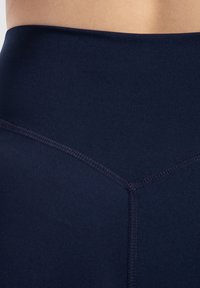 Zbliżenie dolnej części pleców i talii osoby noszącej ciemnoniebieskie, wysokie, bezszwowe legginsy z widocznym szwem.