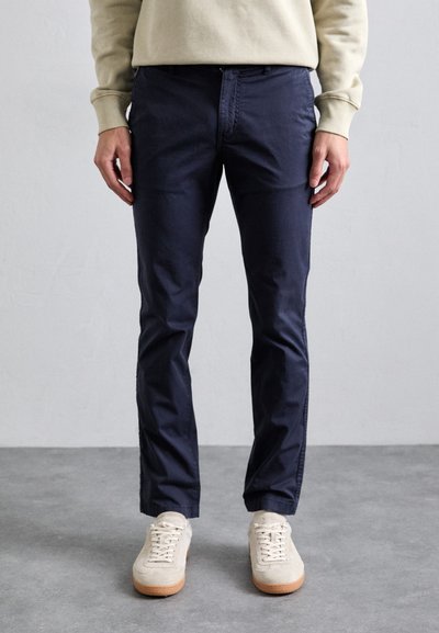 Námořnické modré chinos kalhoty vyrobené z bavlny s úzkým střihem, nabízející klasický design s pěti kapsami a jemnými švy. Stylizováno s lehkými teniskami.