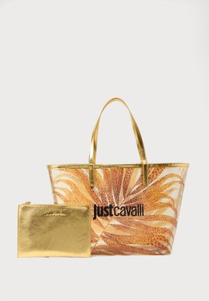 Transparante draagtas met gouden handvaten en bladpatroon, vergezeld van een kleine metalen gouden pouch met het merknaam erin gegraveerd.