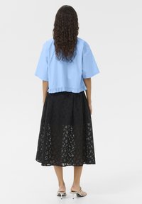Blusa blu corta con orlo arricciato abbinata a una lunga gonna nera in pizzo con motivi geometrici. Sandali con tacco sottile visibili.