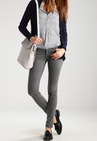 Grå slim-fit-jeans, marinblå kofta, vit mönstrad blus, svarta lackskor och en ljusgrå axelväska. Slätt tyg, skräddarsydd design.