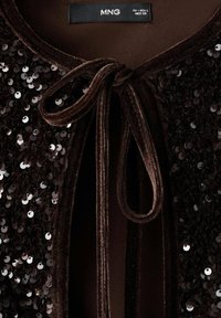 Chaqueta de terciopelo marrón con adornos de lentejuelas negras, con un cierre de lazo en el cuello y un forro interior liso.