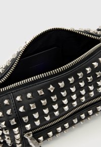 Czarna skórzana kopertówka z srebrnymi piramidkowymi ćwiekami, zamek błyskawiczny oraz tekstylne wykończenie. Wnętrze zawiera ukrytą kieszeń do przechowywania.