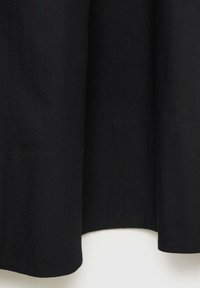 Vêtement en tissu noir avec une texture lisse, présentant un ourlet avec une finition légèrement incurvée et des détails de couture minimalistes.