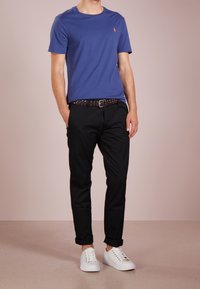 Blå bomulls-T-shirt med kort ärm och en liten logotyp, i kombination med svarta byxor och vita sneakers. Enkelt design och avslappnad passform.