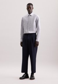 Camicia a maniche lunghe con bottoni e un motivo floreale in colori chiari, abbinata a pantaloni navy a vita alta e scarpe stringate nere.