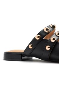 Mocassin en cuir noir avec trois larges brides et des clous métalliques en or rose. Talon carré, semelle plate et finition intérieure lisse.