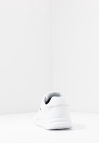 Weiße Sneaker mit einer glatten Lederoberfläche, runder Zehenpartie, gepolstertem Schaftrand und strukturiertem Außensohle. Mit einem kleinen Logo an der Seite.