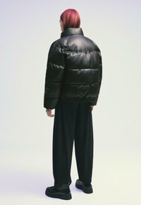 Veste rembourrée en cuir noir avec un design matelassé, col haut et ourlet élastique. Associée à un pantalon noir ample et des chaussures noires imposantes.