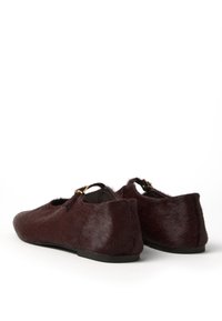 Un paio di scarpe Mary Jane piatte, marroni scure, con texture pelosa e dettagli in oro su sfondo bianco.