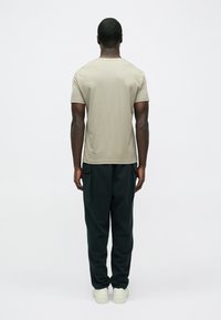 Világos bézs színű rövid ujjú póló sötétzöld cargo nadrággal párosítva. A nadrág oldalán zsebek találhatók, az alján pedig rugalmas szegély.