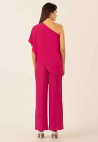 Mono rosa de un solo hombro con pantalones de pierna ancha, que presenta un suave drapeado en el hombro y una textura lisa. Tacones plateados visibles.
