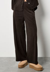 Bruine corduroy wijde broek met een gestructureerd oppervlak. Draag een paar beige platform schoenen met een dikke zool en gestikte details.