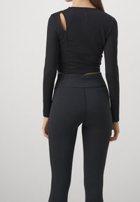 Black long-sleeve cropped top with a cut-out detail and fitted black leggings, both featuring a smooth, stretchy texture.