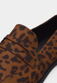 Καφέ παπούτσι loafer με μαύρα λεοπάρ στίγματα, με λουρί πάνω από το επάνω μέρος και μαύρη εσωτερική επένδυση.