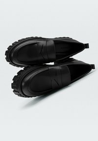 Mocassins noirs en cuir lisse, avec un bout arrondi, un détail de bande élastique et une semelle extérieure rugueuse et texturée.