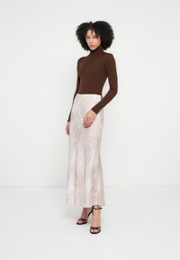 Smeđi rolka s rebrastom teksturom, uparena s dugom, svijetlom suknjom s diskretnim uzorkom životinjskog motiva. Crne sandale s remenčićima.