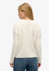 Sweter w kolorze kremowym, wykonany z miękkiego materiału dzianinowego. Posiada opadnięte ramiona, ściągacze przy mankietach i na dole oraz luźny krój.