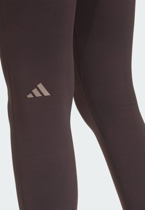 Czarne legginsy sportowe o gładkiej fakturze, z dyskretnym brązowym logo Adidasa na udzie i wzmocnionymi detalami szwów.