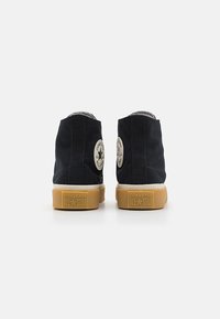 Adidași înalți din pânză neagră, cu talpă din cauciuc, patch cu logo în formă de stea la gleznă și talpă din cauciuc de culoare diferită.