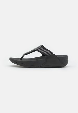 Schwarze Flip-Flops mit einer strukturierten Gummisohle, die einen breiten, gestreiften Stoffriemen und ein kreisförmiges Designelement am Zehensteg aufweisen.