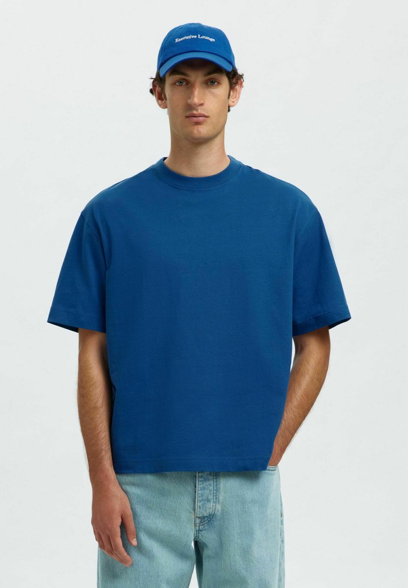 Blå kortærmet t-shirt lavet af bomuld, med rund halsudskæring og afslappet pasform, sammen med en blå kasket med teksten "Executive Lounge".