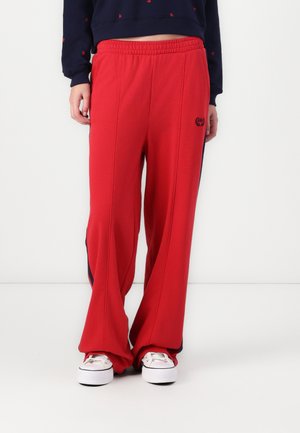 Persoon draagt losse rode trainingsbroek met elastische tailleband en witte sneakers, donkerblauwe cropped sweatshirt boven de taille.