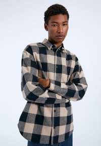 Camisa de manga larga de cuadros en beige y azul marino, con cuello abotonado, textura suave y un patrón de cuadros grande en contraste.