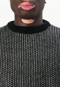 Maglione a righe bianco e nero in maglia con collo a costine, caratterizzato da un tessuto texturizzato e fibre visibili. Inquadratura ravvicinata, senza motivi.