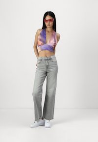Lila och persiko halterneck-topp med djup V-ringning, parat med högmidjade, ljusgrå vida jeans och vita sneakers. Klara rosa solglasögon.